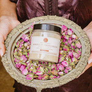 Moroccan Tbrima Blend Herbal Skin Mask, held in a tray of rose petals, highlighting its organic ingredients and skin benefits.