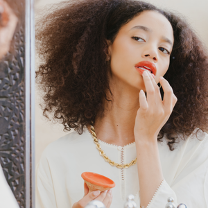 Applying organic lip color from a Moroccan clay pot, using natural ingredients for a personalized shade and smooth finish.