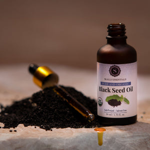 Skalli Essentials Black Seed Oil bottle positioned next to a pile of black seeds, highlighting the organic ingredients used in the product.