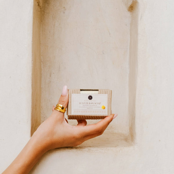 Hand holding Sulfur Bar Soap with Moroccan Argan Oil by Skalli Essentials, showcasing compact packaging and natural skincare lifestyle setting.