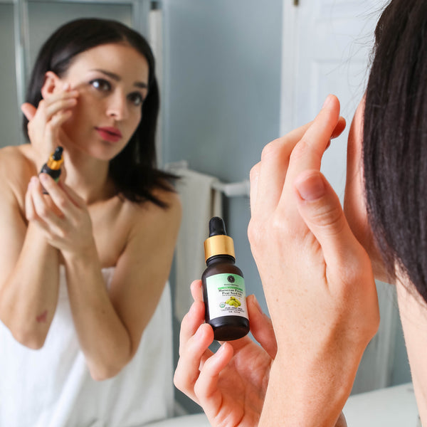 Woman applying Moroccan Prickly Pear Seed Oil in front of a mirror, a natural anti-wrinkle, brightening, and hydrating oil for smoother, youthful skin.