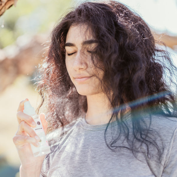 Model applying Skalli Essentials Moroccan Rose Water as a facial mist outdoors, with sunlight illuminating the fine mist and the model's glowing skin.